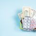 A small shopping basket containing cash and various medication packs against a light blue background.
