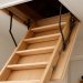 A wooden loft ladder partially extended into an attic space with visible support hardware.