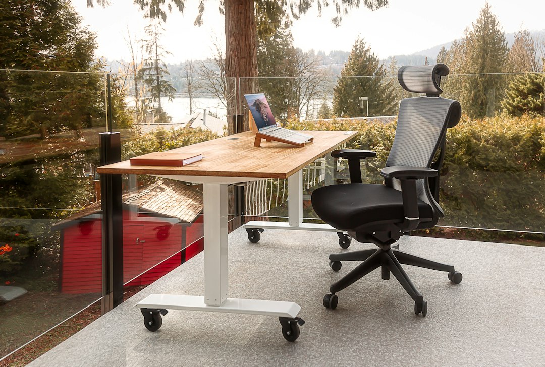 An ergonomic desk setup featuring a wooden standing desk and an ergonomic chair with a scenic view in the background.